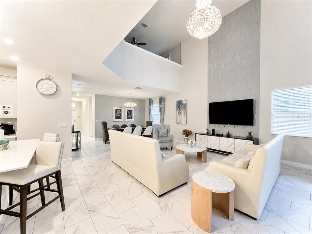 An open-concept living and dining area features high ceilings, white tile floors, and modern furniture — 1585 FLANGE DRIVE, DAVENPORT, FL