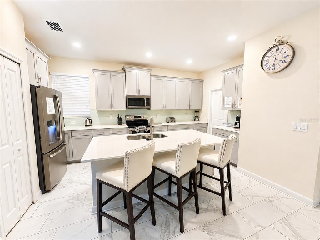 A modern kitchen features light gray cabinetry, a white quartz island, and white marble-look flooring — 1585 FLANGE DRIVE, DAVENPORT, FL