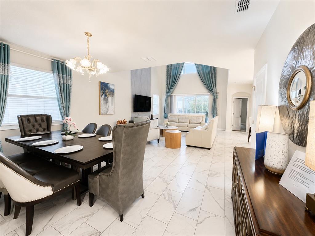 A dining area with a dark table and chairs opens into a bright living room — 1585 FLANGE DRIVE, DAVENPORT, FL