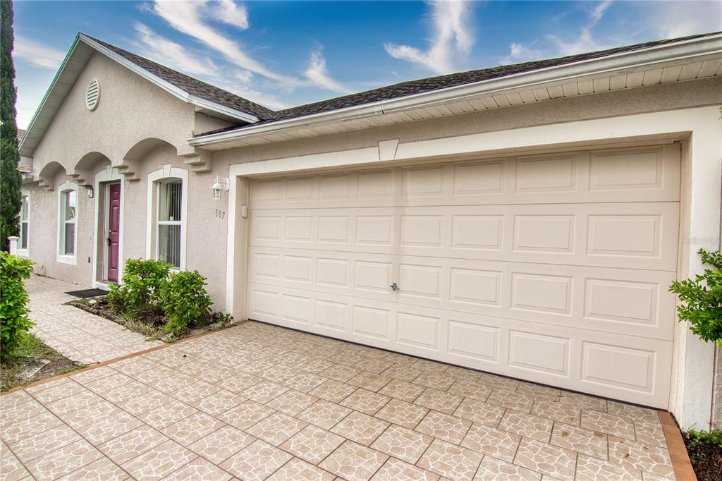 A beige house exterior features a two-car garage, a tiled driveway, and a front entrance — 107 FLATFISH COURT, POINCIANA, FL