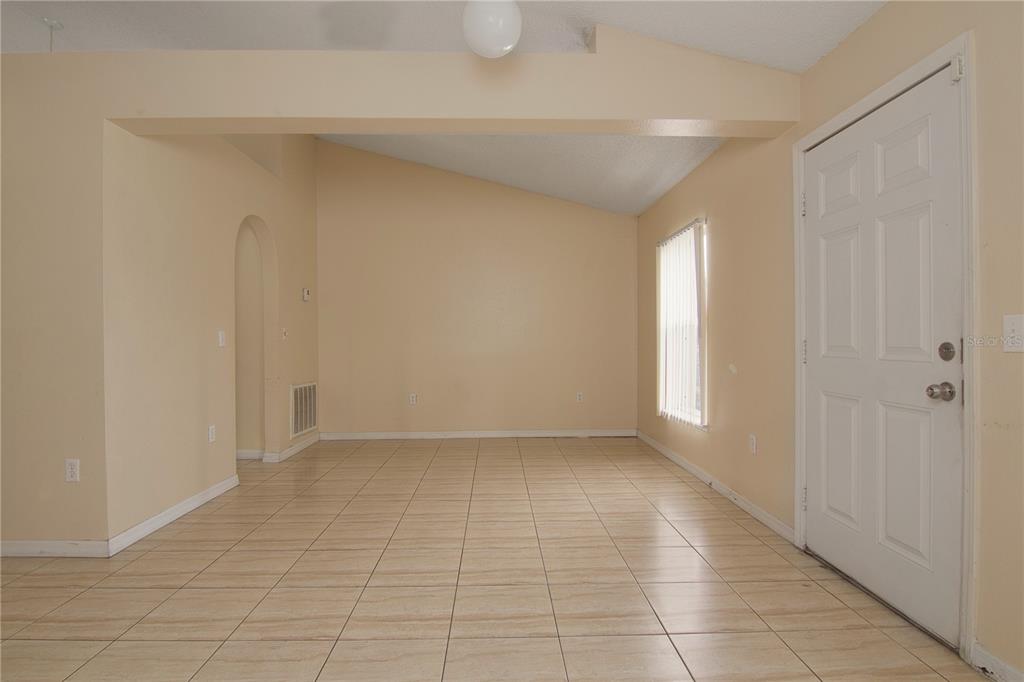 An empty room with beige walls, tile flooring, a vaulted ceiling, and a white door — 107 FLATFISH COURT, POINCIANA, FL