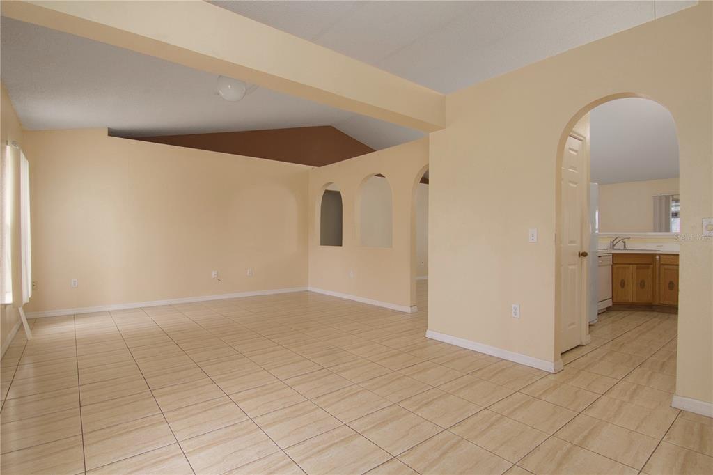 An empty living room with beige tile floors, peach walls, and arched wall openings — 107 FLATFISH COURT, POINCIANA, FL