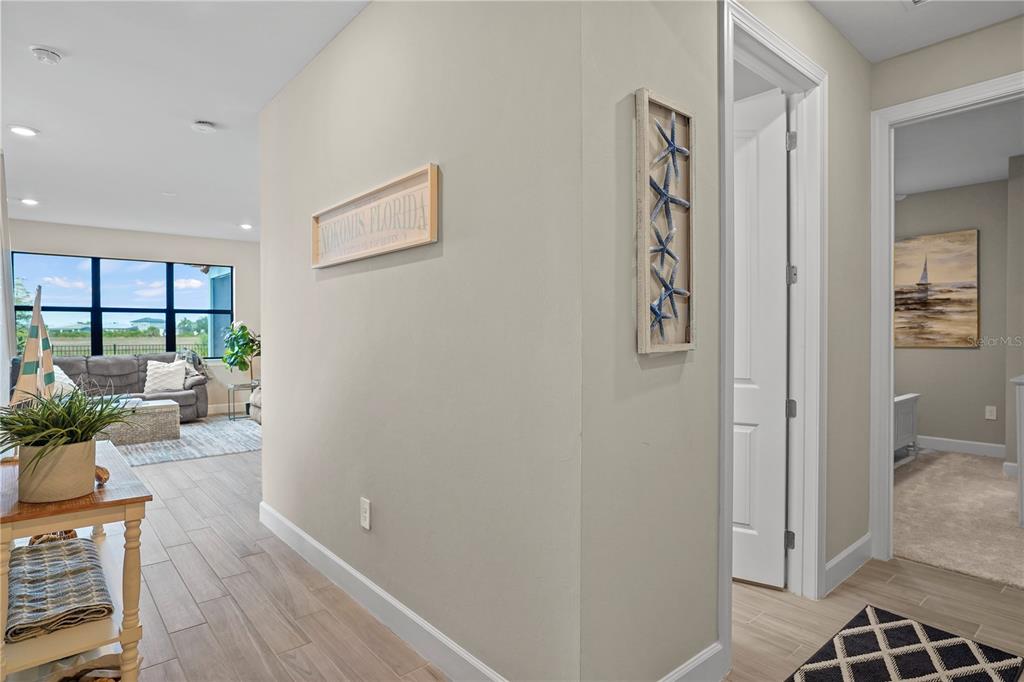 A hallway with light wood-look tile flooring leads to a living area and bedroom — 6288 WINDING PINE DRIVE, NOKOMIS, FL