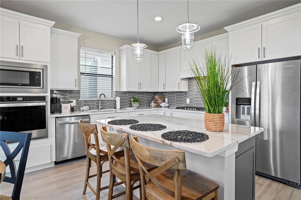 A modern kitchen features white cabinetry, stainless steel appliances, a marble-topped island, and gray backsplash — 6288 WINDING PINE DRIVE, NOKOMIS, FL