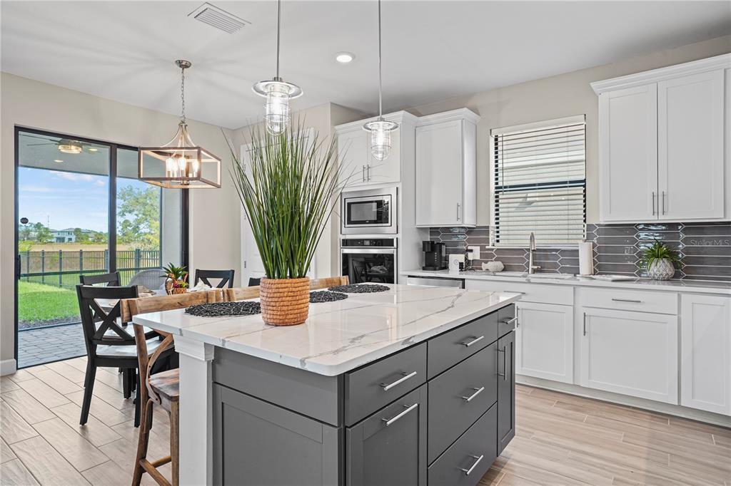 A kitchen with a dark gray island, white cabinets, and a view of a backyard — 6288 WINDING PINE DRIVE, NOKOMIS, FL