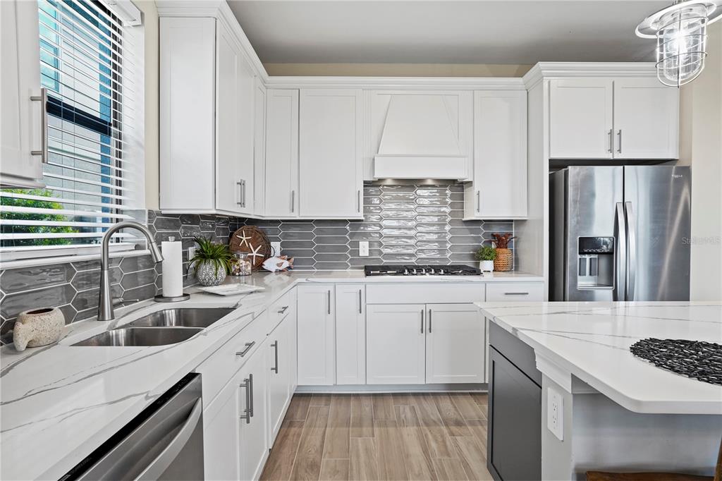 A modern kitchen features white cabinets, gray tile backsplash, stainless steel appliances, and quartz countertops — 6288 WINDING PINE DRIVE, NOKOMIS, FL