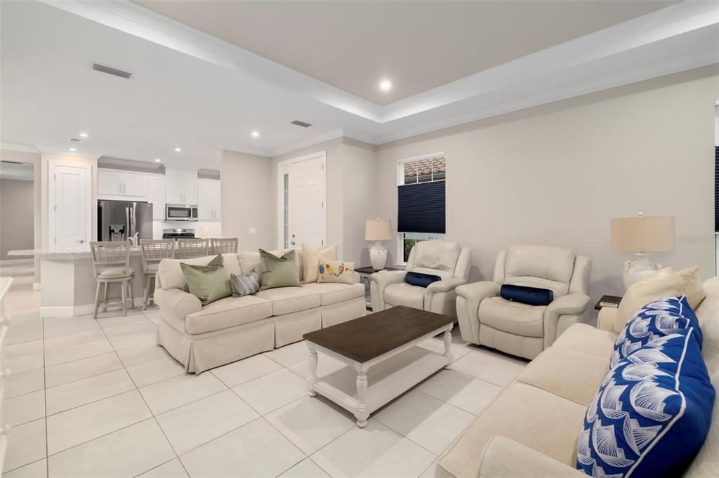 A living room with light tile floors, a beige sofa, two armchairs, and a kitchen — 4759 MOTTA COURT, BRADENTON, FL