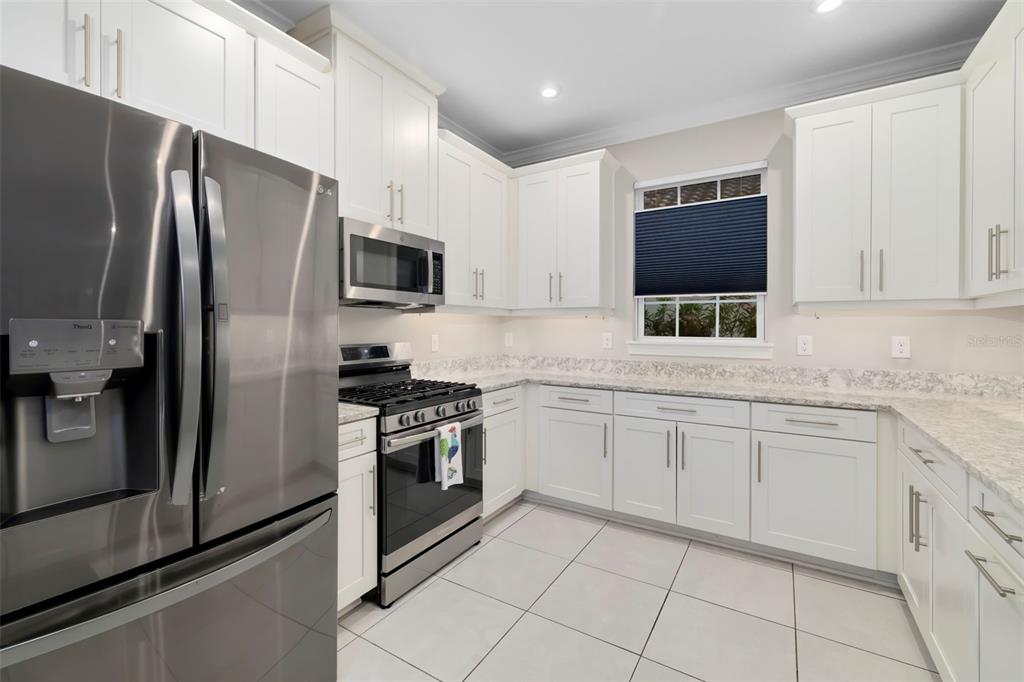 A modern kitchen features white cabinetry, stainless steel appliances, and light-colored granite countertops — 4759 MOTTA COURT, BRADENTON, FL