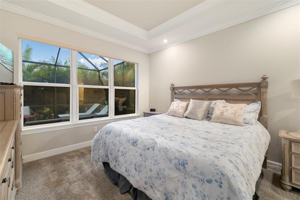 A bedroom features a bed with a floral comforter, a tray ceiling, and large windows — 4759 MOTTA COURT, BRADENTON, FL