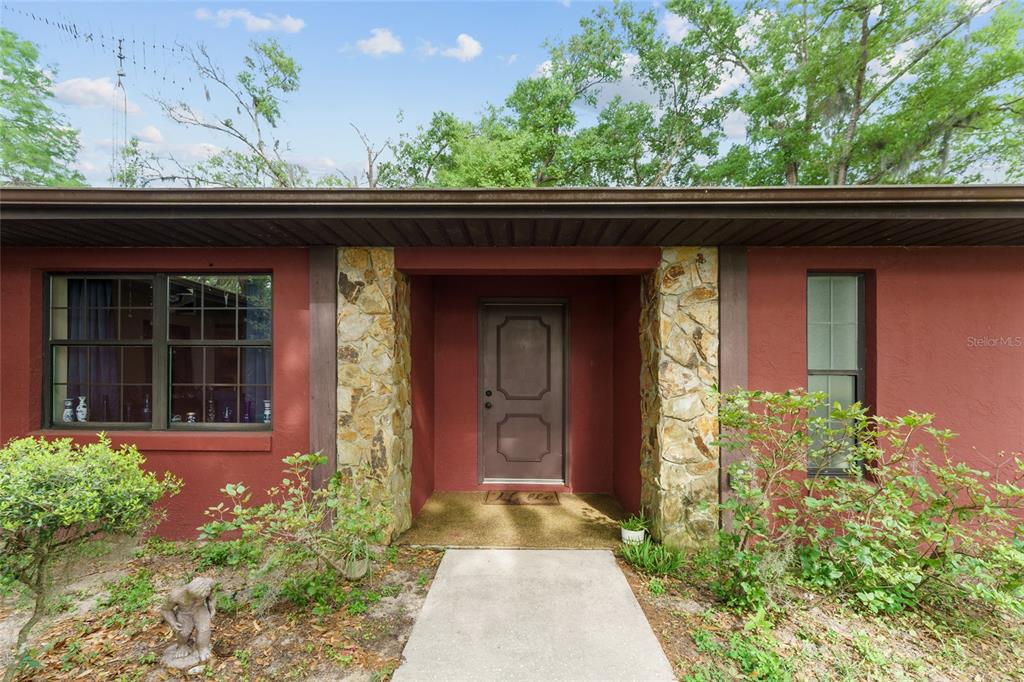 The exterior of a house features a red stucco facade, stone accents, and a front door — 3149 SW 200TH AVENUE, DUNNELLON, FL