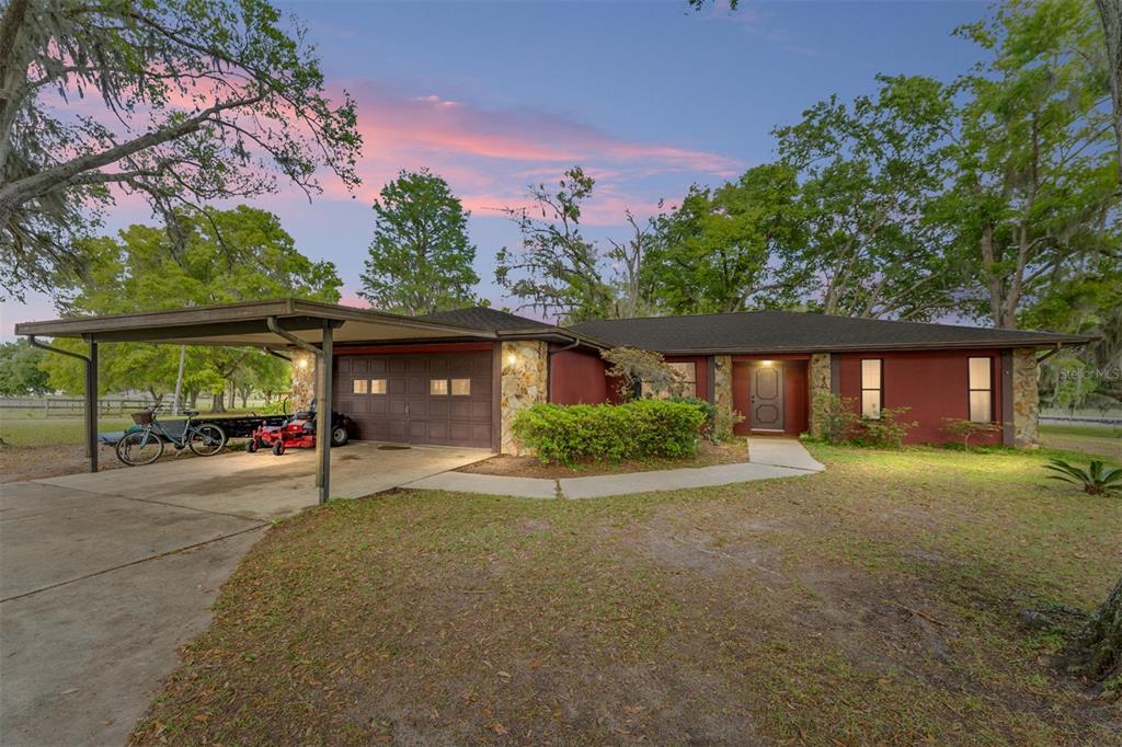 A single-story house with a carport, stone accents, and a red exterior at dusk — 3149 SW 200TH AVENUE, DUNNELLON, FL
