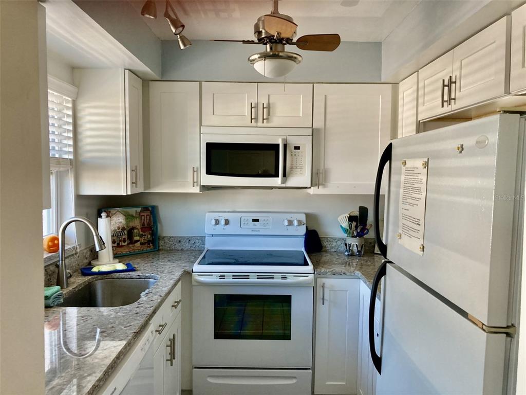 A kitchen features white cabinets, granite countertops, a white stove, and a white refrigerator — 304 47TH AVENUE DRIVE W UNIT 307, BRADENTON, FL