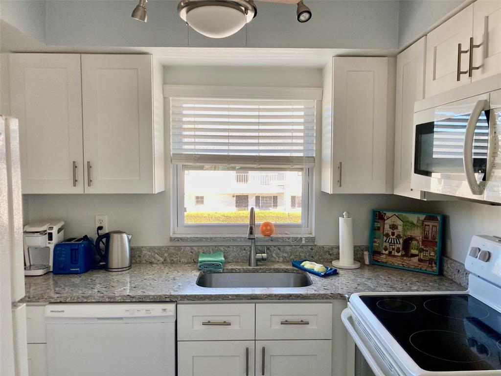 A kitchen features white cabinets, granite countertops, a stainless steel sink, and a window view — 304 47TH AVENUE DRIVE W UNIT 307, BRADENTON, FL