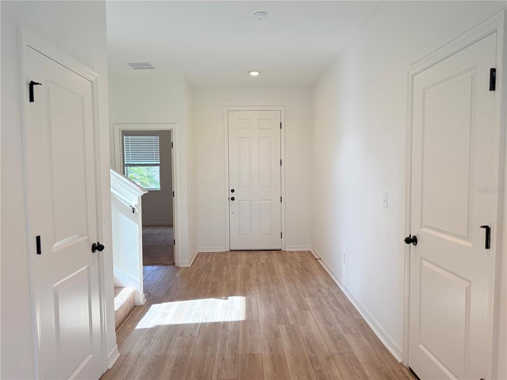 A bright entryway features light wood-look flooring, white walls, two closed doors, and a staircase — 9544 SANDY BLUFFS CIRCLE, PARRISH, FL