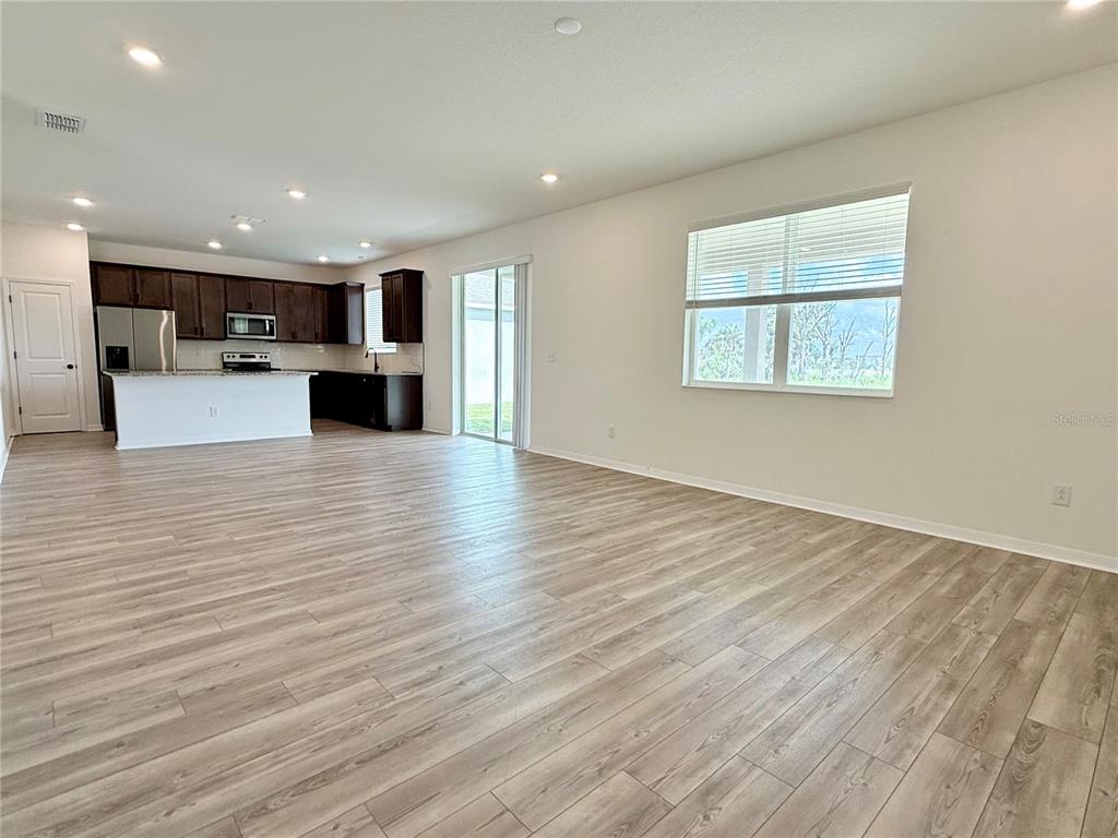 An open-concept living area features wood-look flooring, a kitchen with dark cabinets, and sliding doors — 9544 SANDY BLUFFS CIRCLE, PARRISH, FL