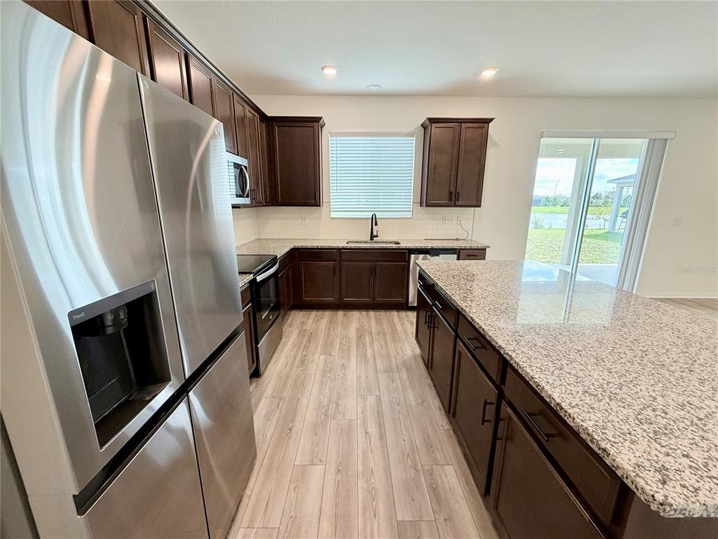 A kitchen features dark wood cabinets, granite countertops, stainless steel appliances, and light wood flooring — 9544 SANDY BLUFFS CIRCLE, PARRISH, FL