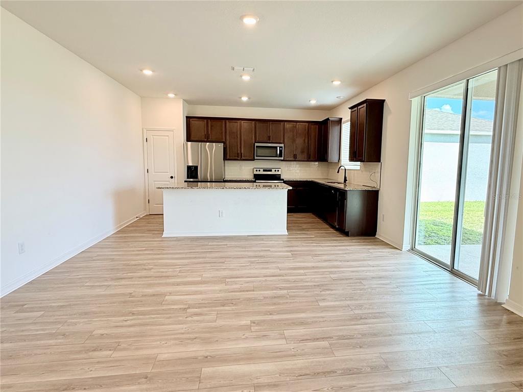 A kitchen with dark wood cabinets, granite countertops, and stainless steel appliances opens to a living area — 9544 SANDY BLUFFS CIRCLE, PARRISH, FL