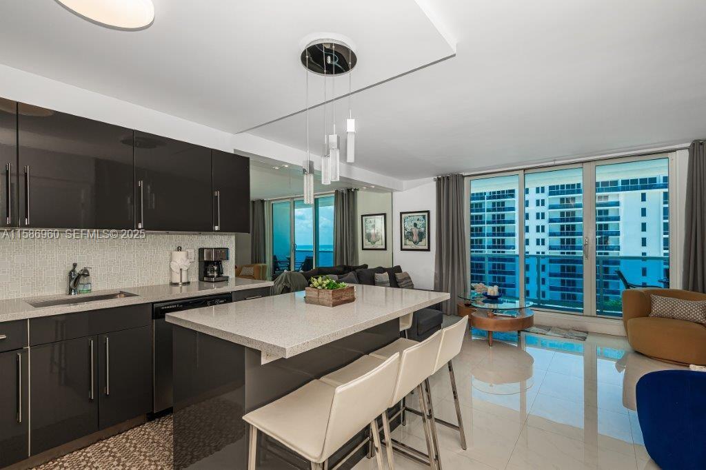 A modern kitchen with dark cabinets and a stone island overlooks a bright living area — 2301 Collins Ave # 1111, Miami Beach FL 33139, MIAMI BEACH, FL
