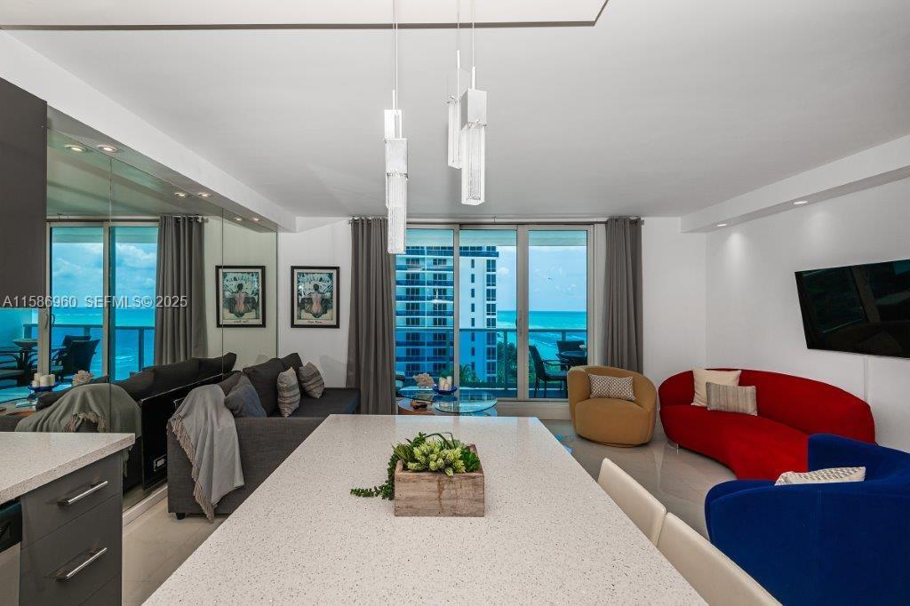 A modern living room and kitchen area features a white island, red sofa, and ocean views — 2301 Collins Ave # 1111, Miami Beach FL 33139, MIAMI BEACH, FL