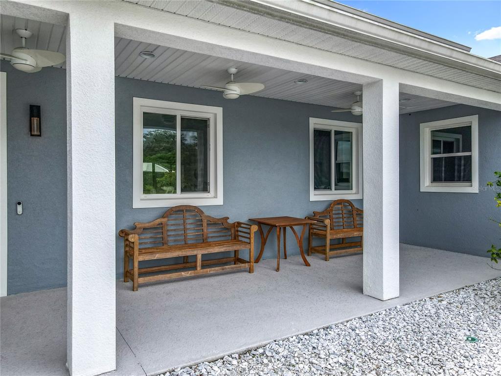 A covered patio features gray stucco walls, white columns, ceiling fans, and two wooden benches — 10224 BAY LAKE ROAD, GROVELAND, FL