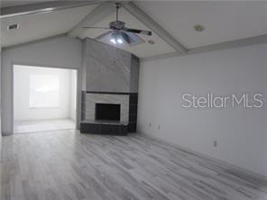 A living room with light wood-look flooring, a vaulted ceiling, and a corner stone fireplace — 305 COBLE DRIVE, LONGWOOD, FL