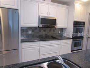 A kitchen features white cabinetry, stainless steel appliances, and dark granite countertops — 305 COBLE DRIVE, LONGWOOD, FL