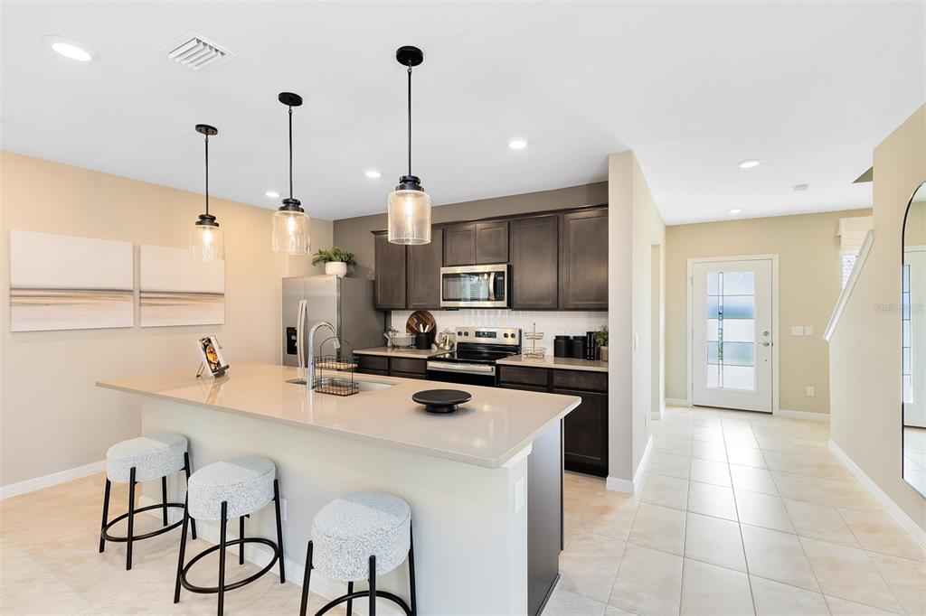 A kitchen features dark cabinets, a light-colored island with bar stools, and tile flooring — 5099 STARLING BIRD LANE, ST CLOUD, FL