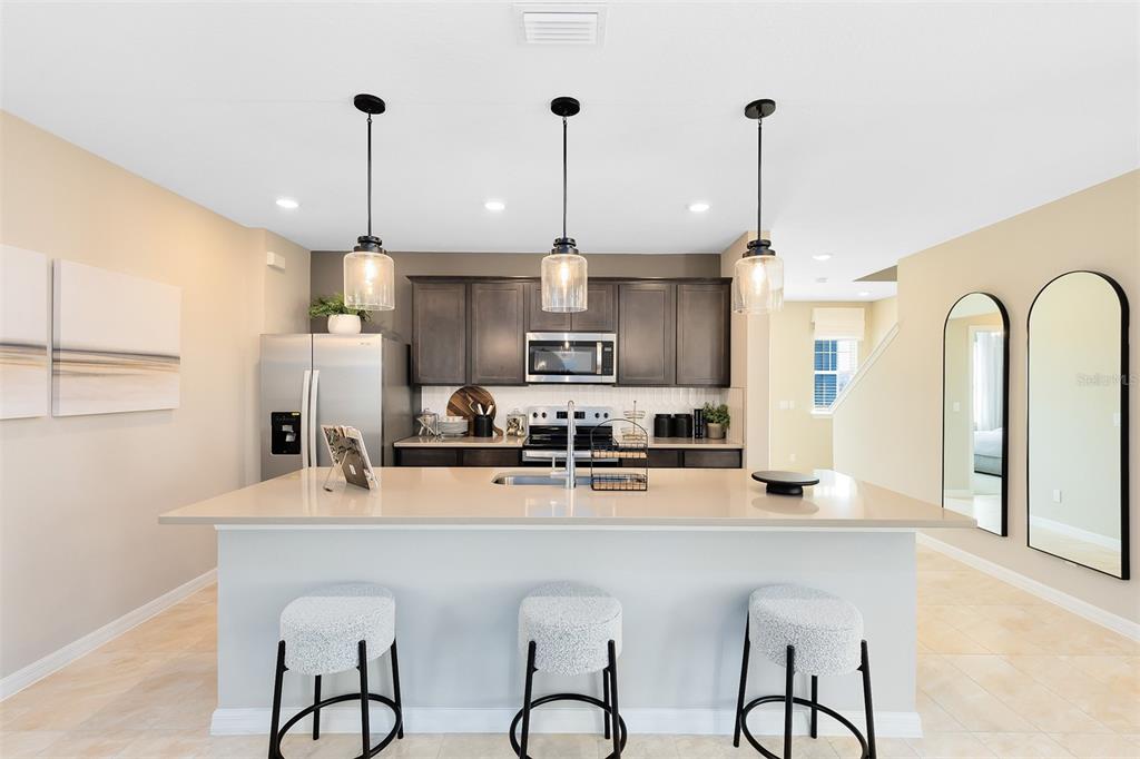 A kitchen with a large island, three bar stools, dark cabinets, and three pendant lights — 5099 STARLING BIRD LANE, ST CLOUD, FL