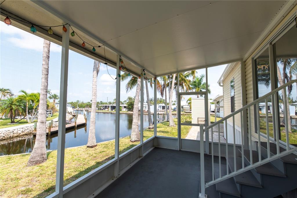 A screened-in porch overlooks a canal with palm trees and a wooden dock — 23 HOLLAND DRIVE, PUNTA GORDA, FL