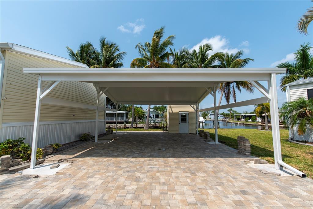 A paved carport with a white metal roof sits beside a house near a canal — 23 HOLLAND DRIVE, PUNTA GORDA, FL