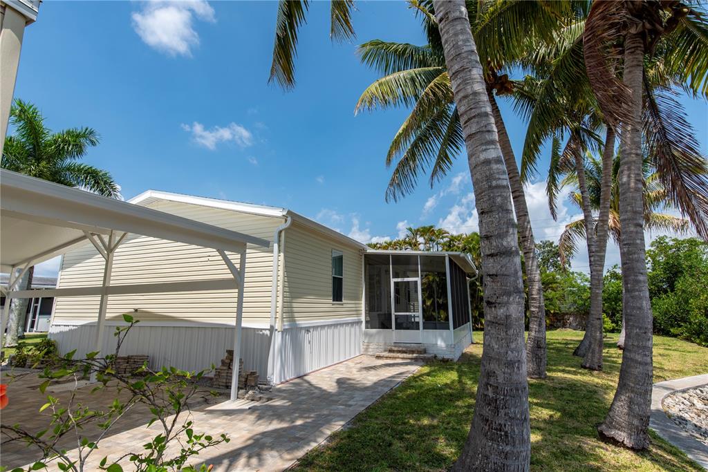 A light-colored mobile home features a screened-in porch, a paved patio, and several palm trees — 23 HOLLAND DRIVE, PUNTA GORDA, FL