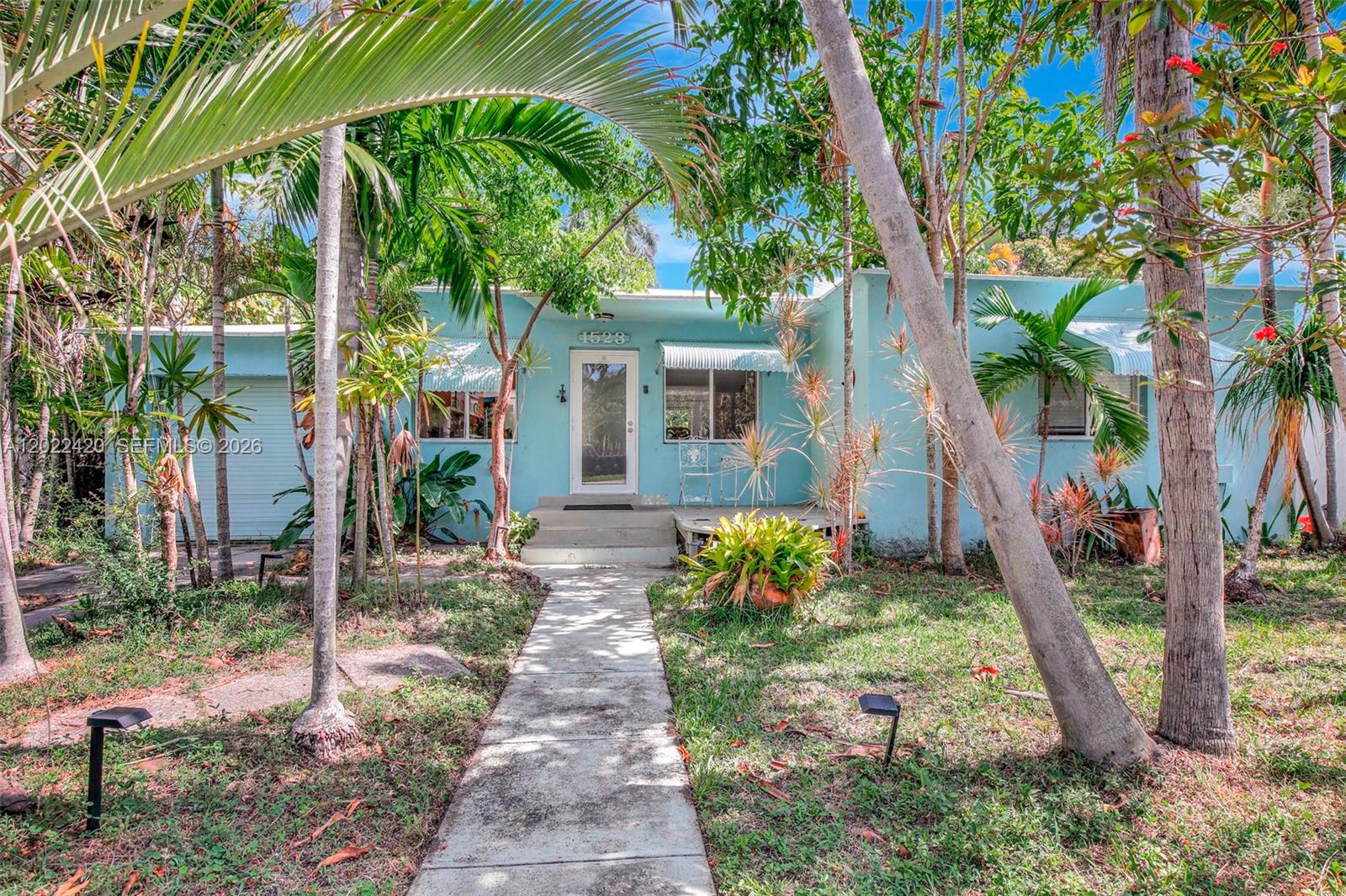 A light blue single-story house with a concrete walkway and lush tropical landscaping — 1523 Dewey St, Hollywood FL 33020, HOLLYWOOD, FL