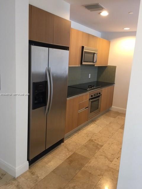 A galley kitchen features light wood cabinets, stainless steel appliances, and beige tile flooring — 1060 BRICKELL AV # 1901, Miami FL 33131, MIAMI, FL