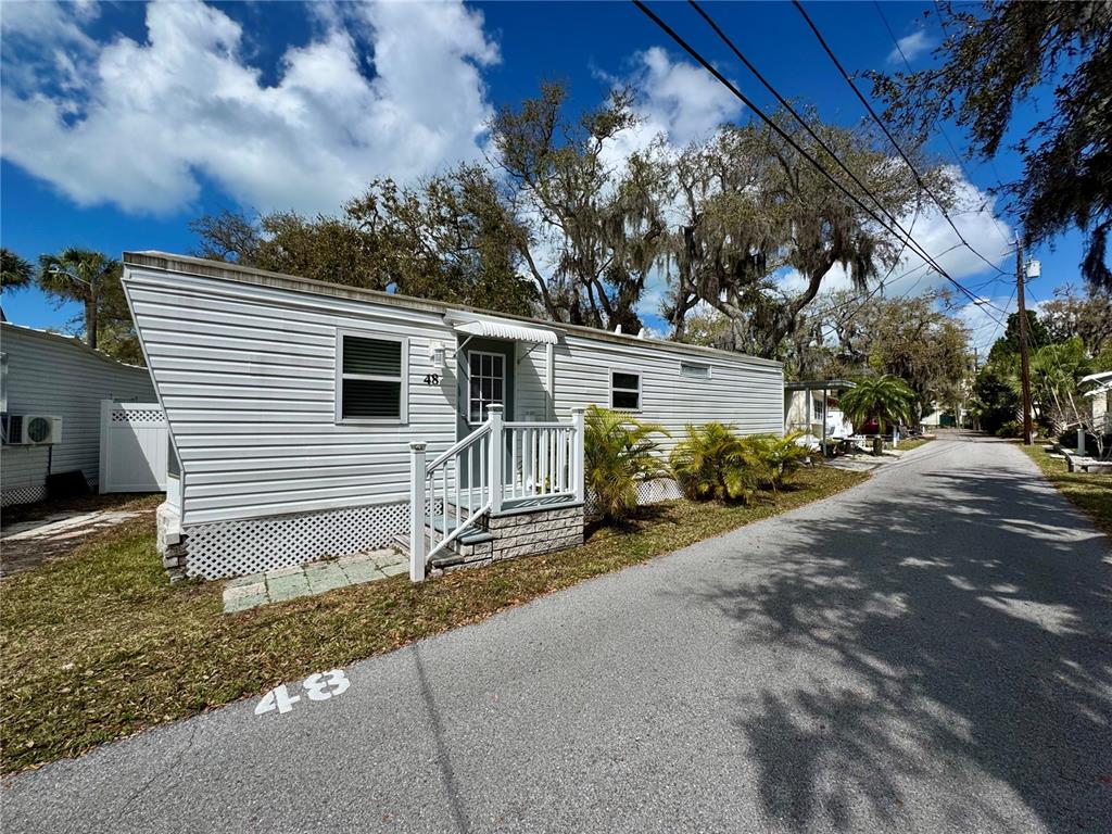 A white mobile home with a small front porch sits along a paved street — 15010 113TH AVENUE N UNIT 48, LARGO, FL