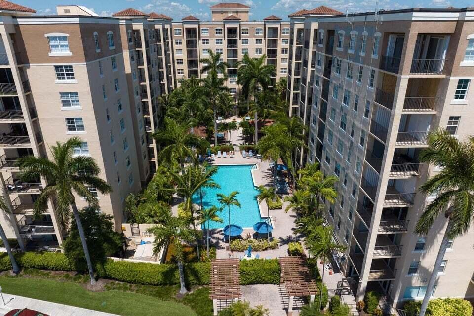 An aerial view of a swimming pool surrounded by palm trees and multi-story apartment buildings — 1805 N Flagler Drive # 107, West Palm Beach FL 33407, WEST PALM BEACH, FL