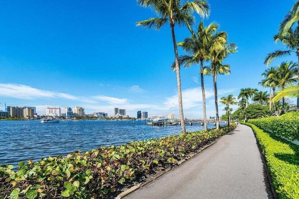 A paved path runs alongside a waterfront with palm trees and a distant city skyline — 1805 N Flagler Drive # 107, West Palm Beach FL 33407, WEST PALM BEACH, FL