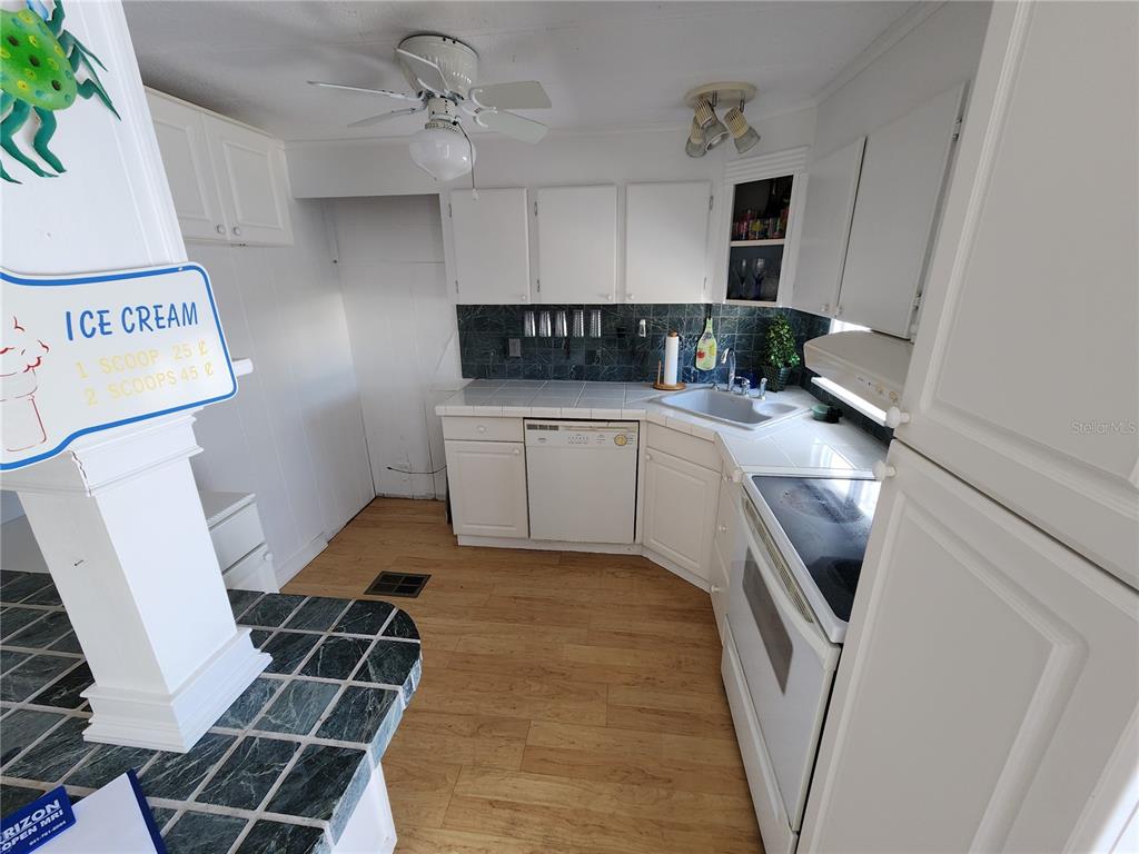 A kitchen features white cabinets, a dark tiled backsplash, light wood flooring, and white appliances — 305 BATAN COURT, BRADENTON, FL