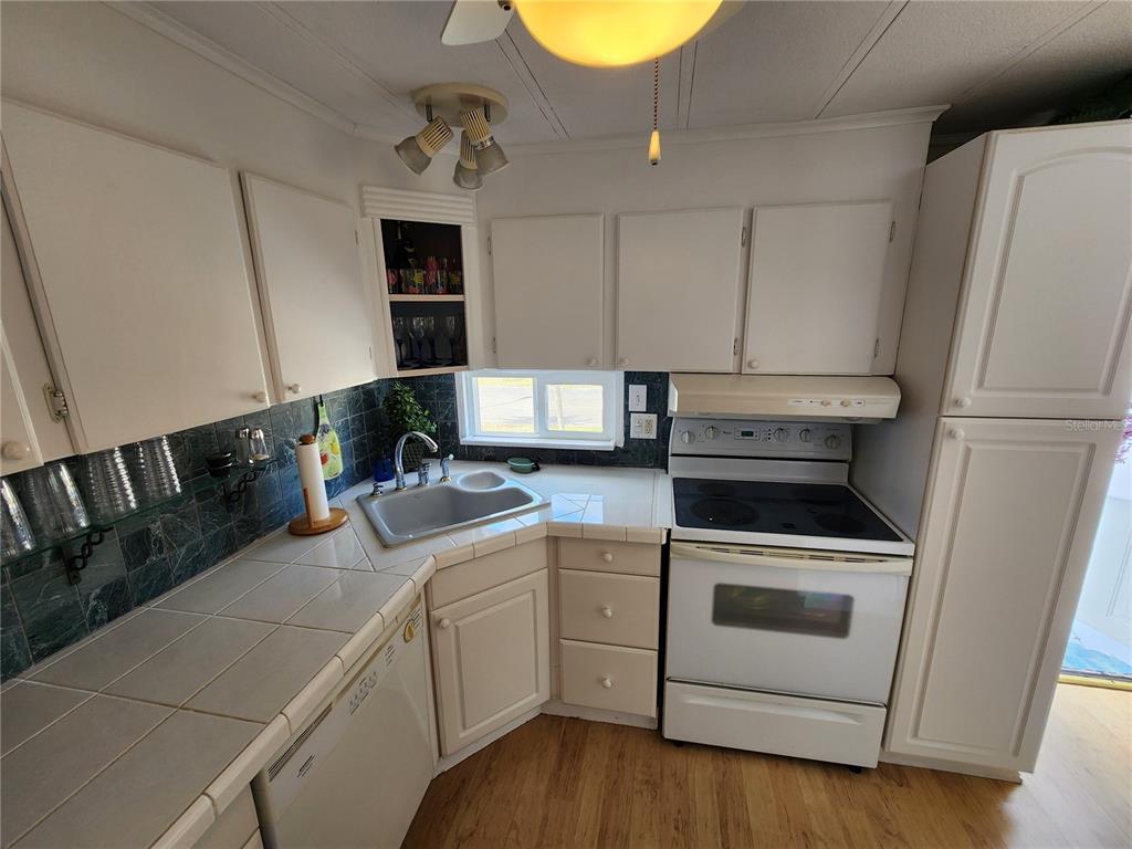 A kitchen features white cabinets, a corner sink, tiled countertops, and white appliances — 305 BATAN COURT, BRADENTON, FL