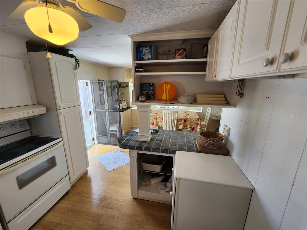 A kitchen features white cabinets, a tiled peninsula counter, and a view into a dining area — 305 BATAN COURT, BRADENTON, FL