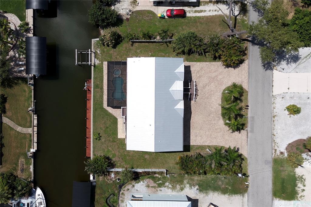 An aerial view shows a waterfront house with a metal roof, pool cage, and dock — 9150 PINE COVE DRIVE, ENGLEWOOD, FL