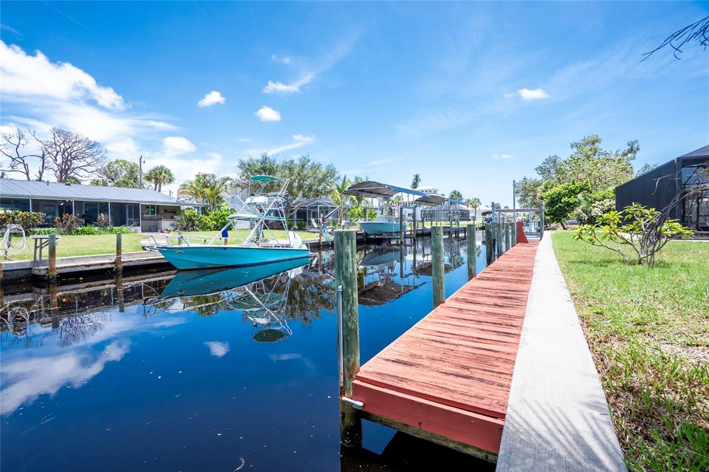 A wooden dock extends into a canal with two boats moored alongside a grassy yard — 9150 PINE COVE DRIVE, ENGLEWOOD, FL