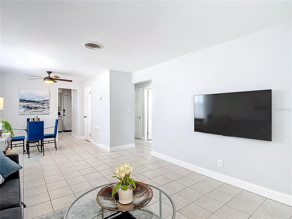A living room with tile flooring, a wall-mounted television, and an adjacent dining area — 220 SE JEFFERSON CIRCLE N, ST PETERSBURG, FL