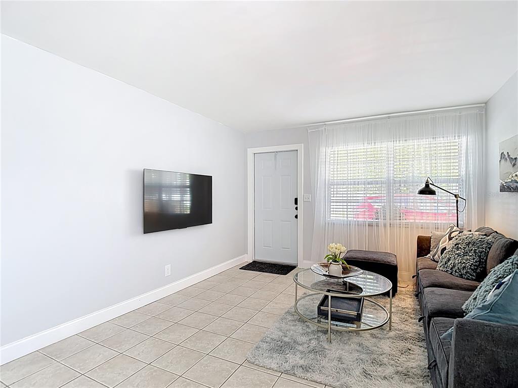 A living room features a wall-mounted television, tiled flooring, a gray sofa, and a front door — 220 SE JEFFERSON CIRCLE N, ST PETERSBURG, FL