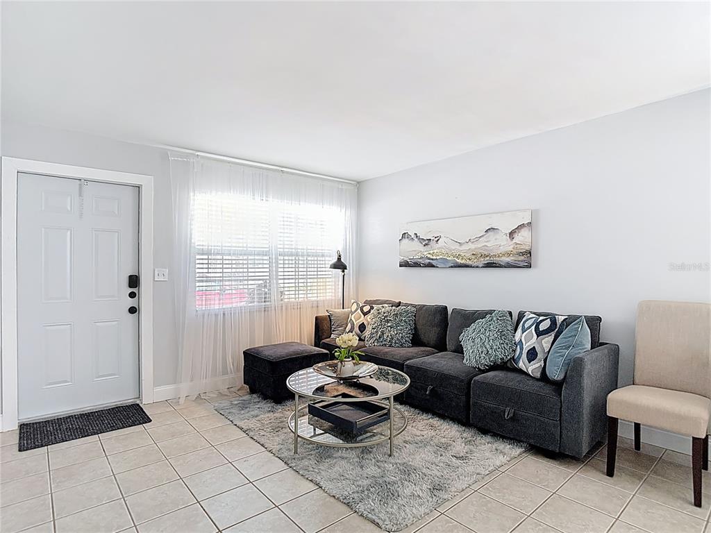 A living room features a gray sectional sofa, a glass coffee table, and tile flooring — 220 SE JEFFERSON CIRCLE N, ST PETERSBURG, FL