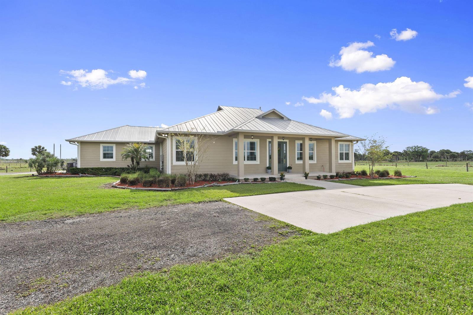 A tan, single-story house with a metal roof sits on a large, grassy lot — 1720 S Brocksmith Road, Fort Pierce FL 34945, FORT PIERCE, FL