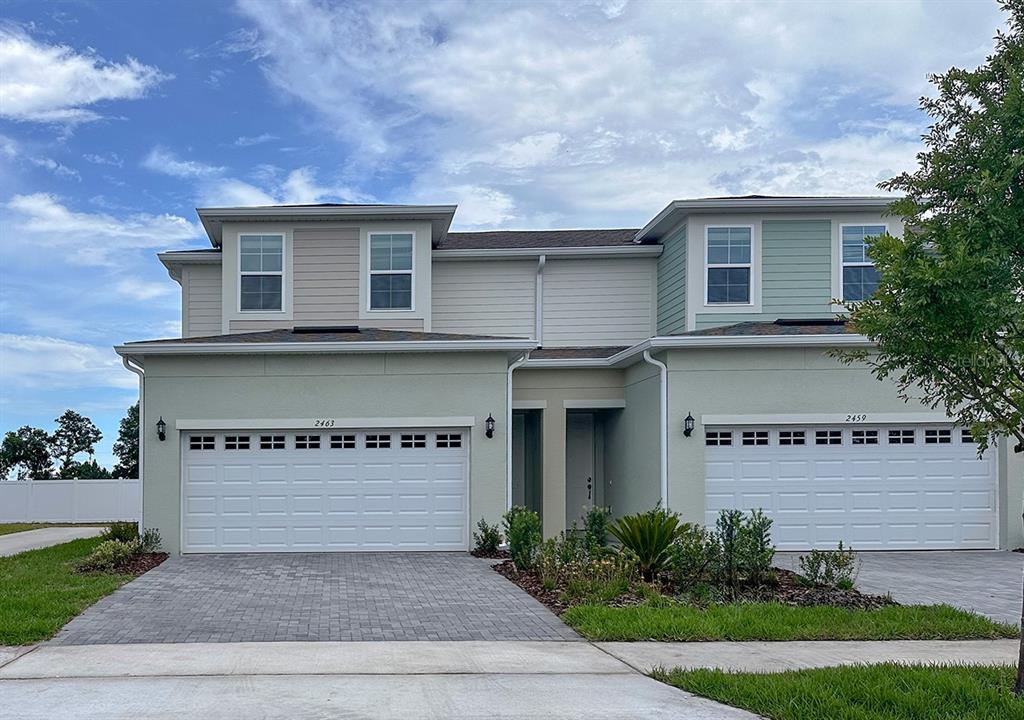 A two-story duplex with light-colored siding, two white garage doors, and a shared entryway — 24101 MANUMA STREET UNIT Seminole 2508, ST CLOUD, FL