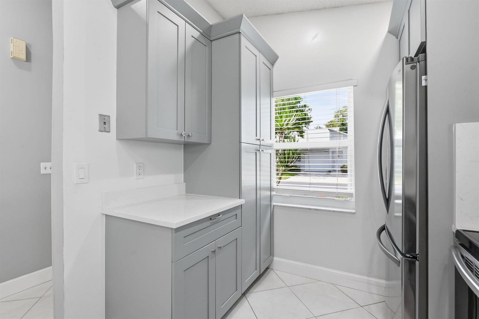 A kitchen area features gray cabinets, white countertops, a window, and a stainless steel refrigerator — 8621 Jasmine Way, Boca Raton FL 33496, BOCA RATON, FL
