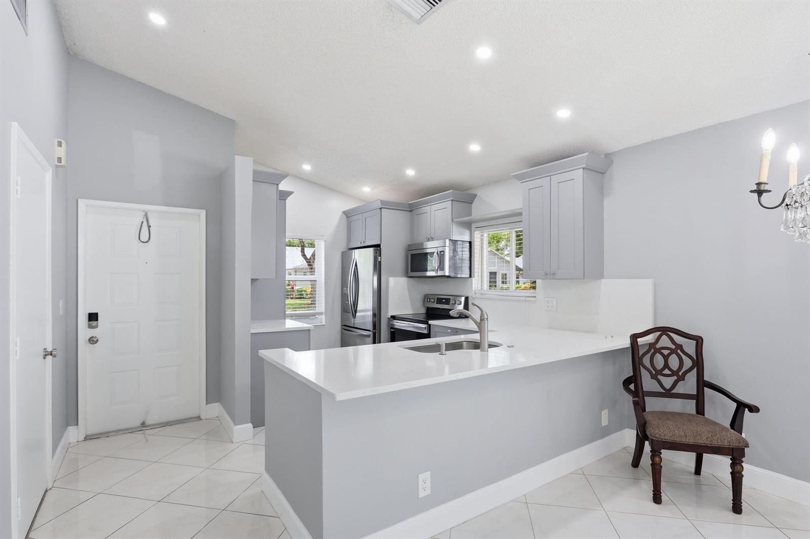 A kitchen with light gray cabinets, white countertops, and tile flooring features a breakfast bar — 8621 Jasmine Way, Boca Raton FL 33496, BOCA RATON, FL