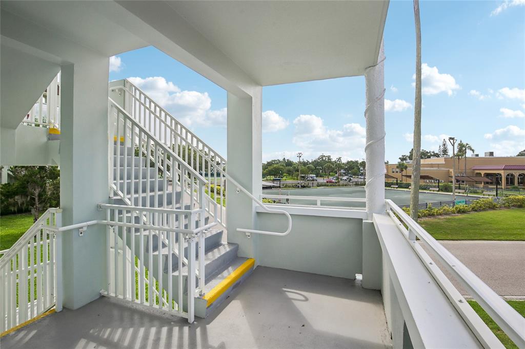 An outdoor stairwell with white railings leads to a covered landing overlooking a tennis court — 2380 WORLD PARKWAY BOULEVARD UNIT 40, CLEARWATER, FL