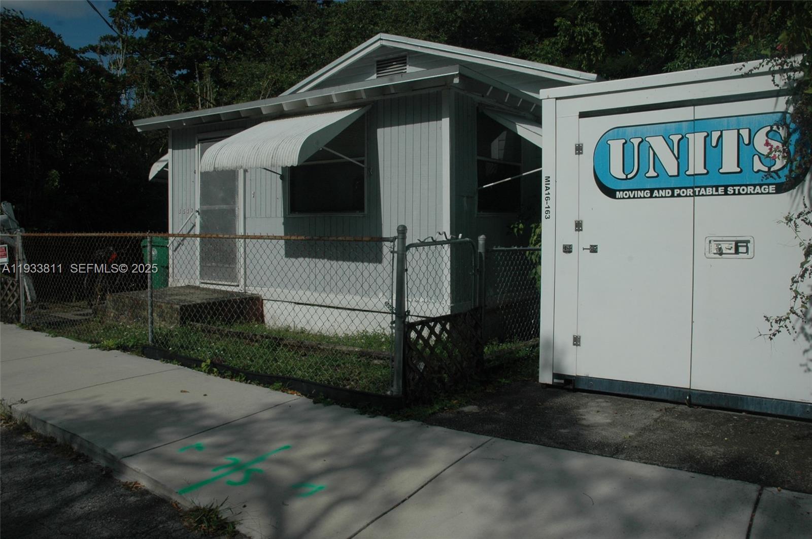 A small, light-colored house sits behind a chain-link fence next to a portable storage container — 3537 Charles Ave, Miami FL 33133, MIAMI, FL